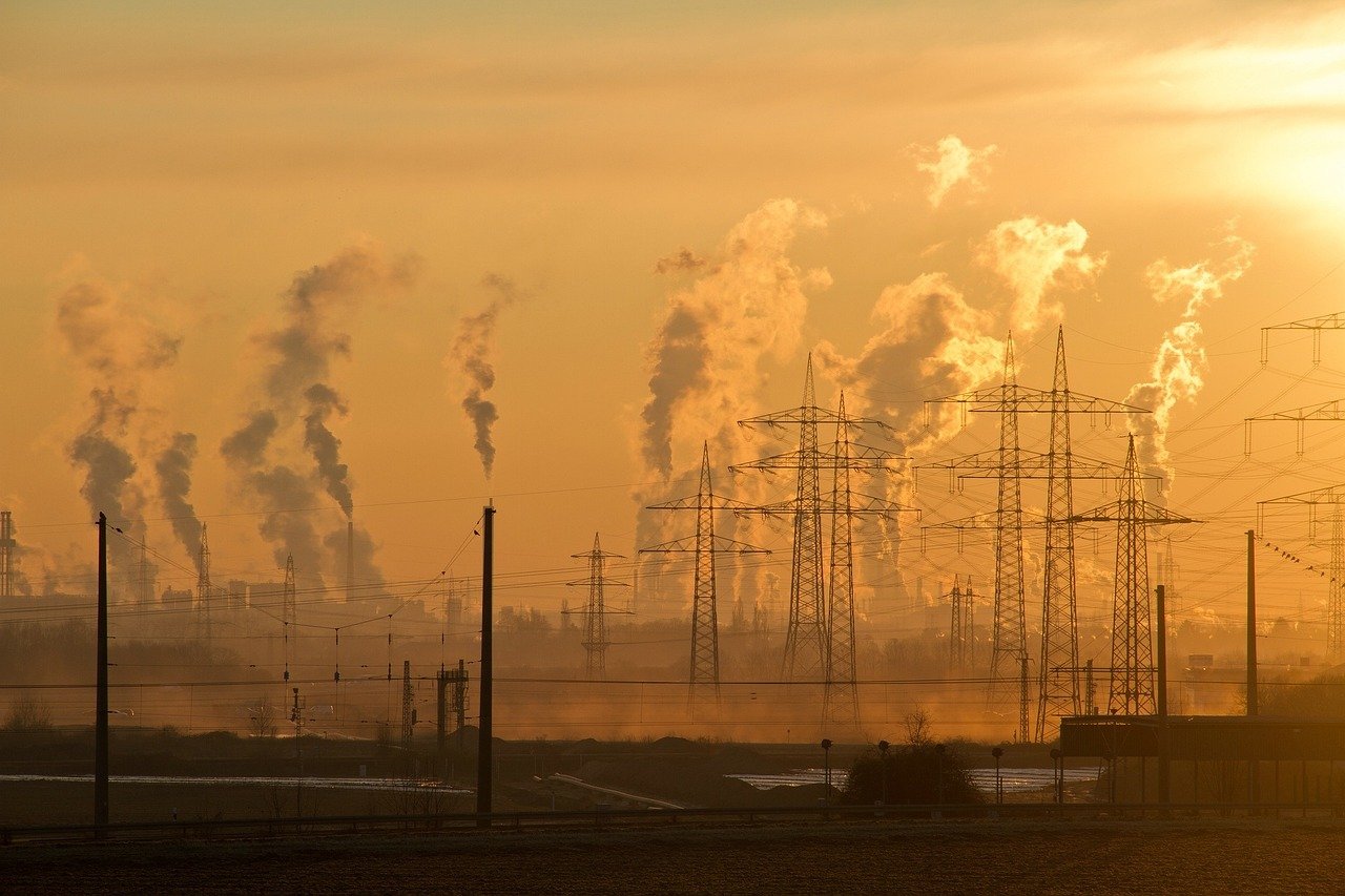 A large industrial facility with multiple smokestacks emitting visible emissions into the sky